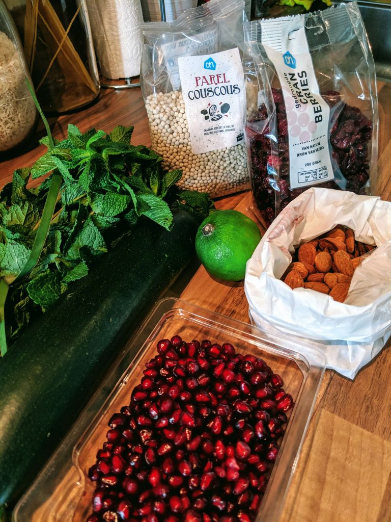 de ingrediënten voor deze couscous salade: naast parelcouscous ook verse munt, courgette, granaatappelpitjes, limoen, cranberries en amandelen
